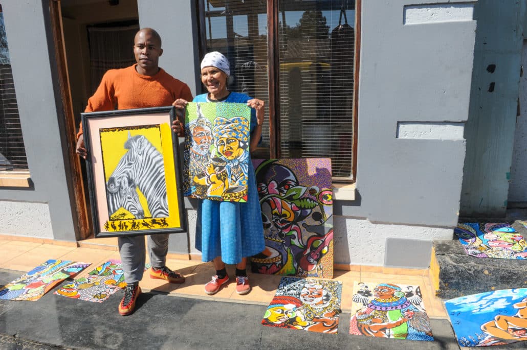 Tumi Masite, left, is an artist who participates in the Maboneng Township Arts Experience, an initiative that invites outsiders inside the homes of artists who showcase their works there. He and his grandmother show off some of his paintings.